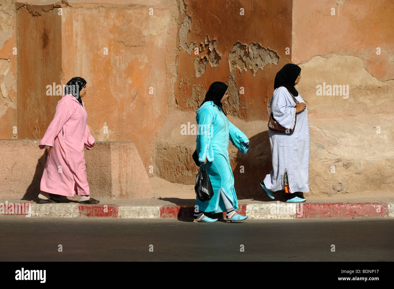 Marokkanische Frauen mit Kopfbedeckungen und Djellabas traditionelle farbenfrohe oder farbenfrohe Bademäntel oder Kostüme spazieren an den Stadtmauern von Marrakesch, Marokko Stockfoto
