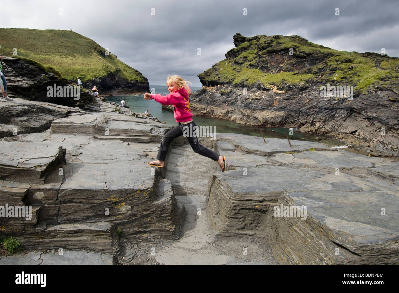 Ein glückliches kleines Mädchen mit blondes Haar springen über Felsen am Eingang zum Hafen von Boscastle in der Nähe von Wadebridge, Cornwall. Stockfoto