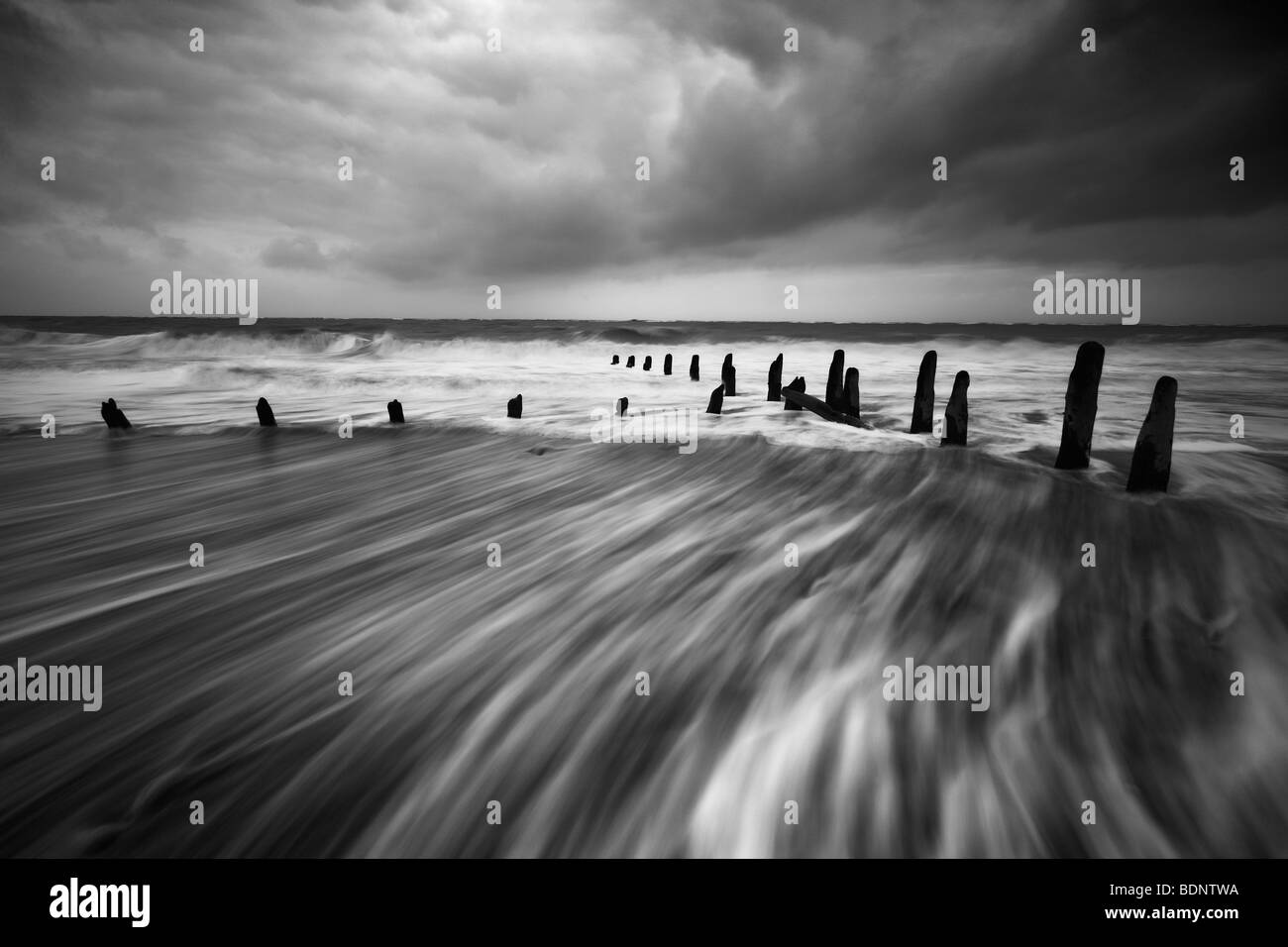 Meerwasser bewegt durch Holz Breakers Wit Gewitterhimmel Stockfoto