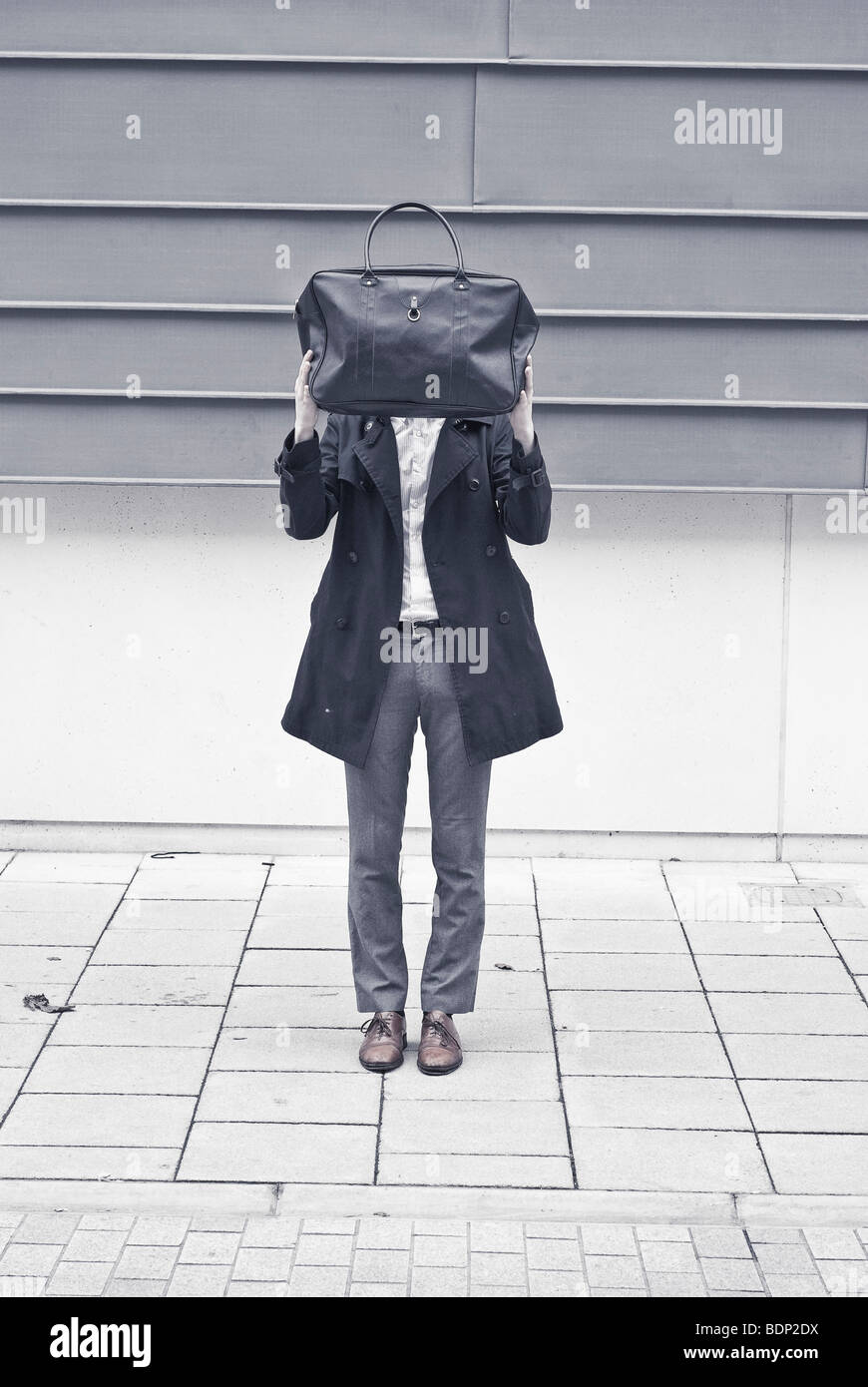 Ein Mann steht auf einer Straße versteckt sich hinter einer Tasche Stockfoto