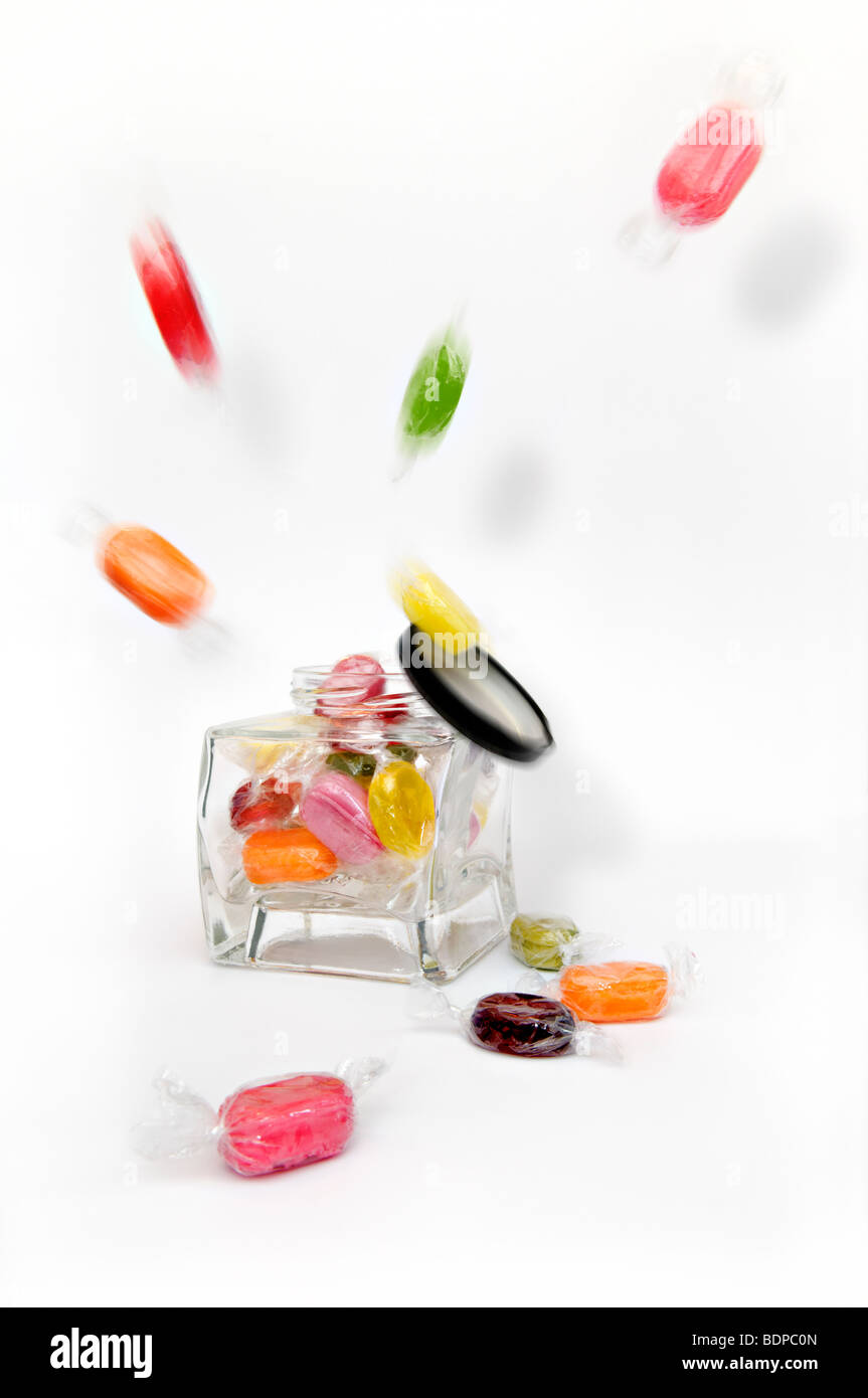 Studioaufnahme von farbigen gekochte fruchtigen Süßigkeiten explodierenden aus Glas vor einen weißen Hintergrund mit Deckel herunterfallen Stockfoto