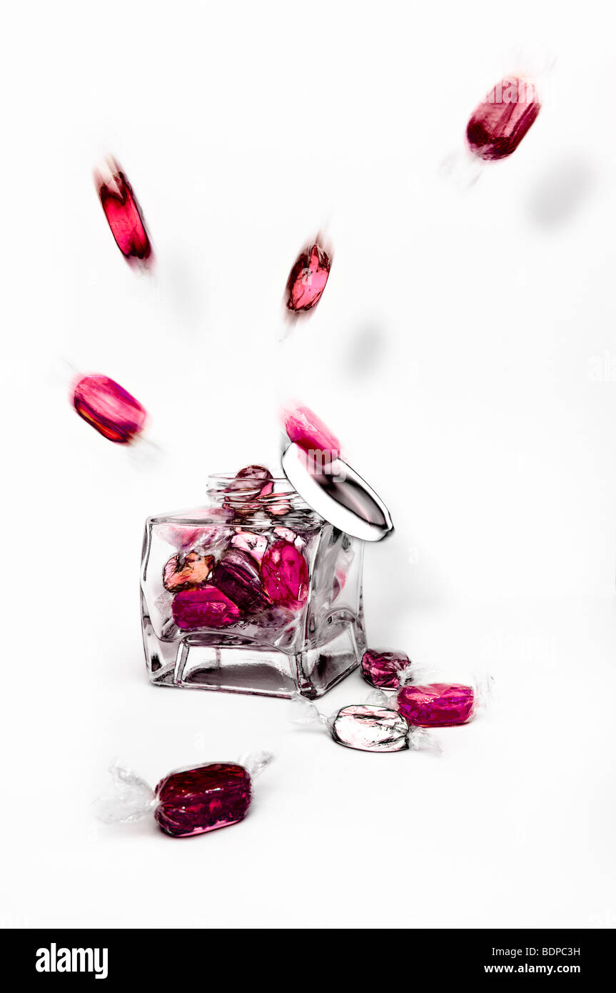 Studio gedreht, rosa und roten gekochte fruchtige Bonbons explodierenden aus Glas vor einen weißen Hintergrund mit Deckel herunterfallen Stockfoto