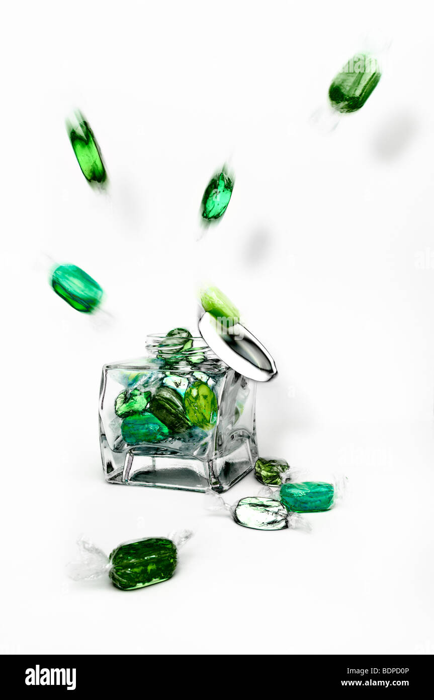 Studioaufnahme grüne gekochte fruchtige Bonbons explodierenden aus Glas vor einen weißen Hintergrund mit Deckel herunterfallen Stockfoto