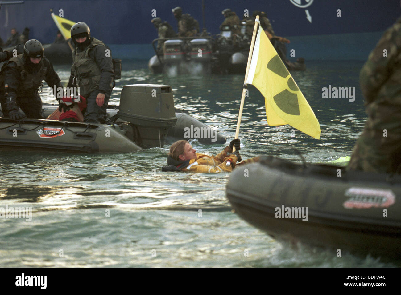 Ein GP-Aktivist im Wasser hält eine Fahne mit dem Symbol der Strahlung. Die Marines sind in Hüpfburgen in der Nähe. Stockfoto