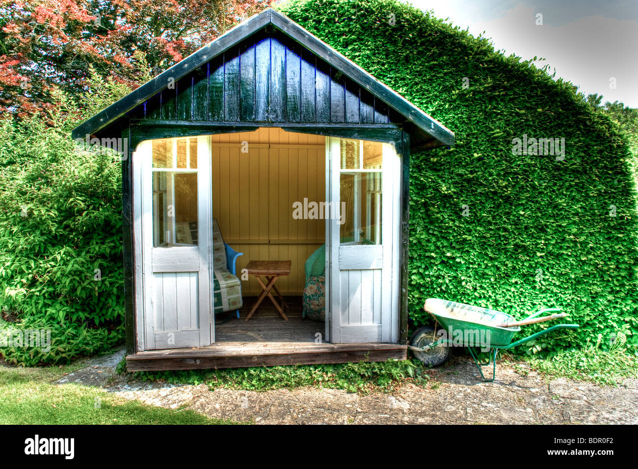 Ein kleine hölzerne Sommer Haus mit Stühlen, Tisch und eine grüne Schubkarre Stockfoto