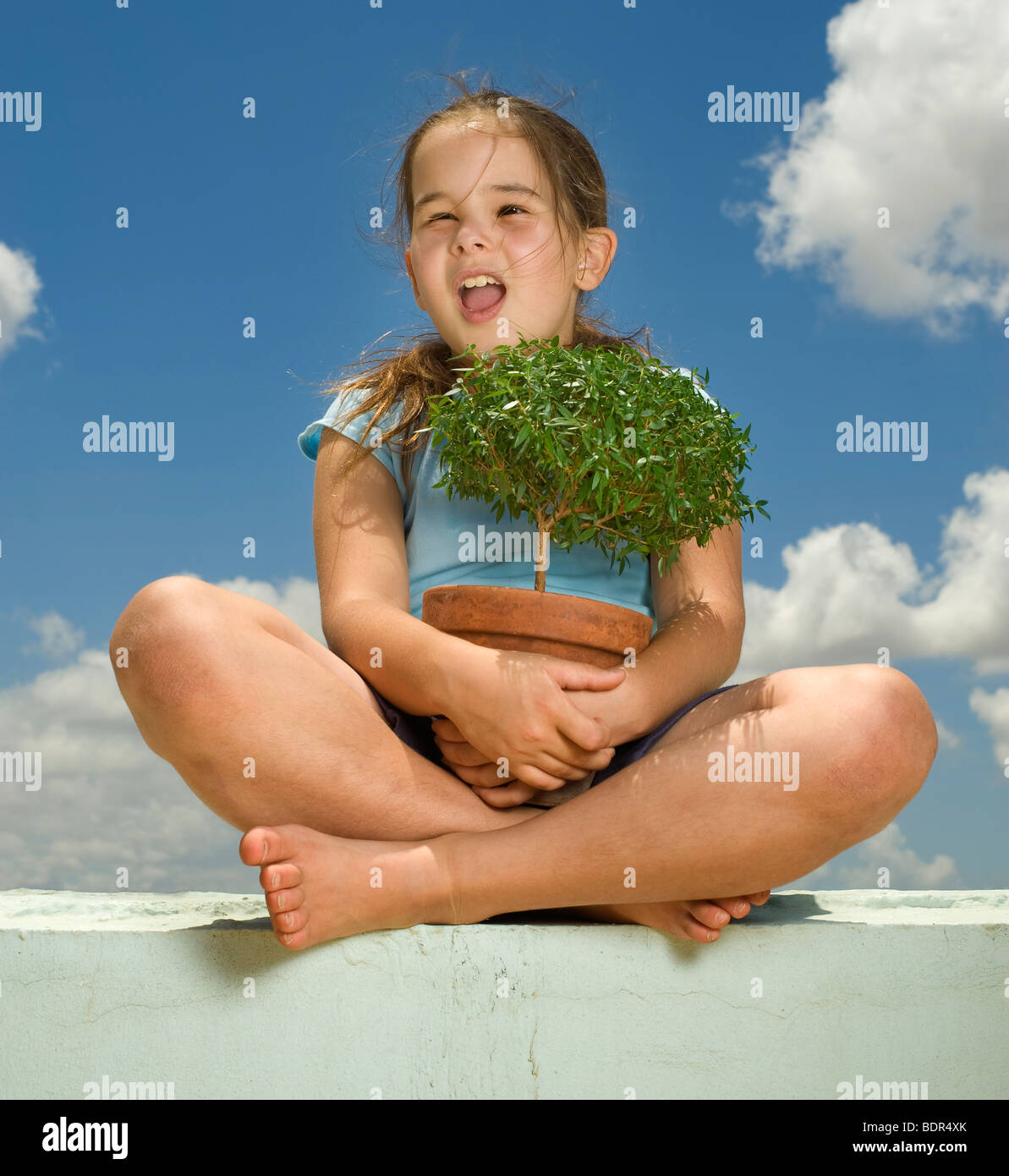 Mädchen mit kleinen Baum gegen blauen Wolkenhimmel Stockfoto