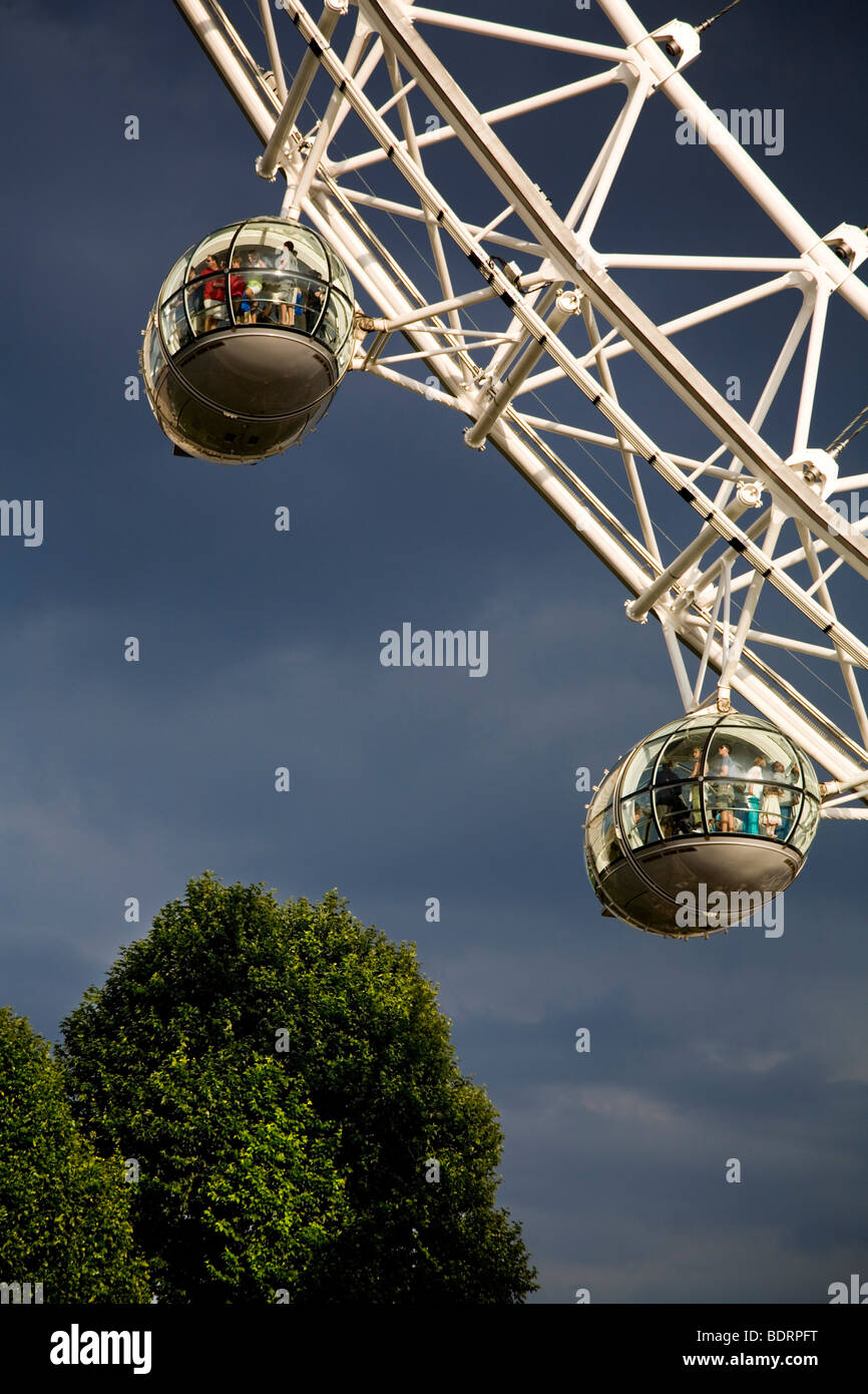 Zwei London Eye Capsoules voller Touristen Gewitterhimmel bewölktem Wetter Teil des Rades über Bäume vertikal Southbank Themse am Flussufer Stockfoto