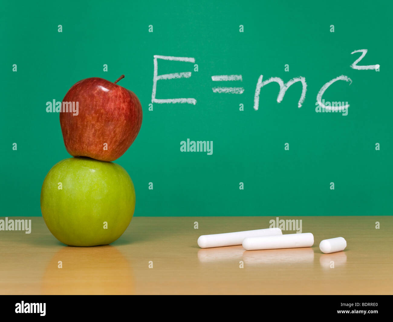 Einsteins Formel der Relativitätstheorie auf einer Kreidetafel. Einige Kreiden und Äpfel im Vordergrund. Stockfoto