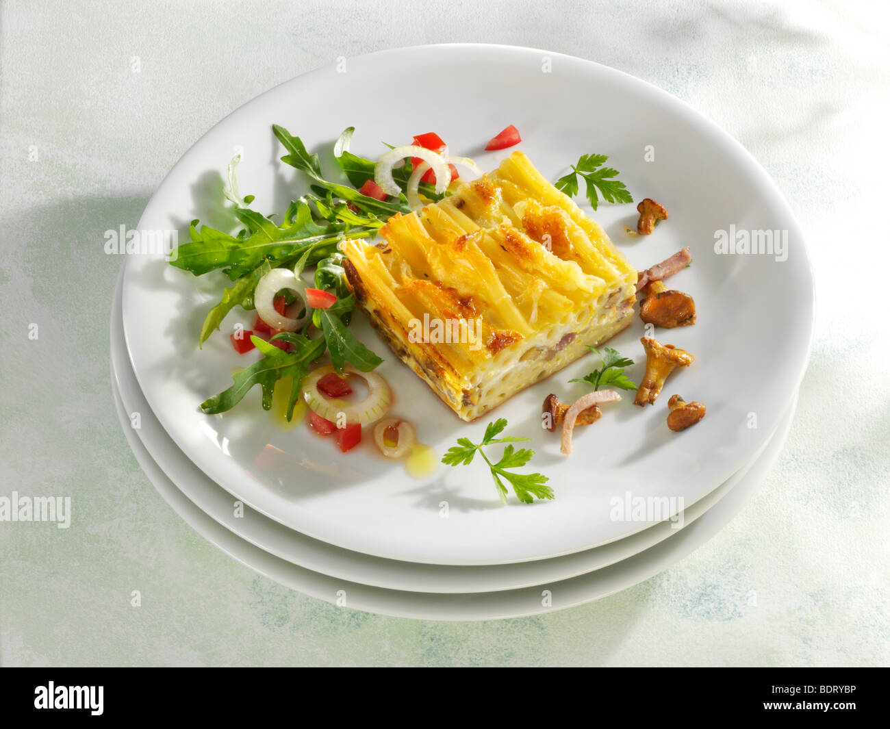 Maccaroni-Gratin mit Pilzen und Rucola-Salat auf einen Stapel von Platten Stockfoto