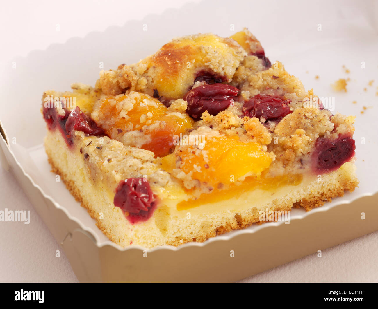 Stück Kuchen mit Aprikosen, Kirschen und Streusel auf einem weißen Papierteller Stockfoto