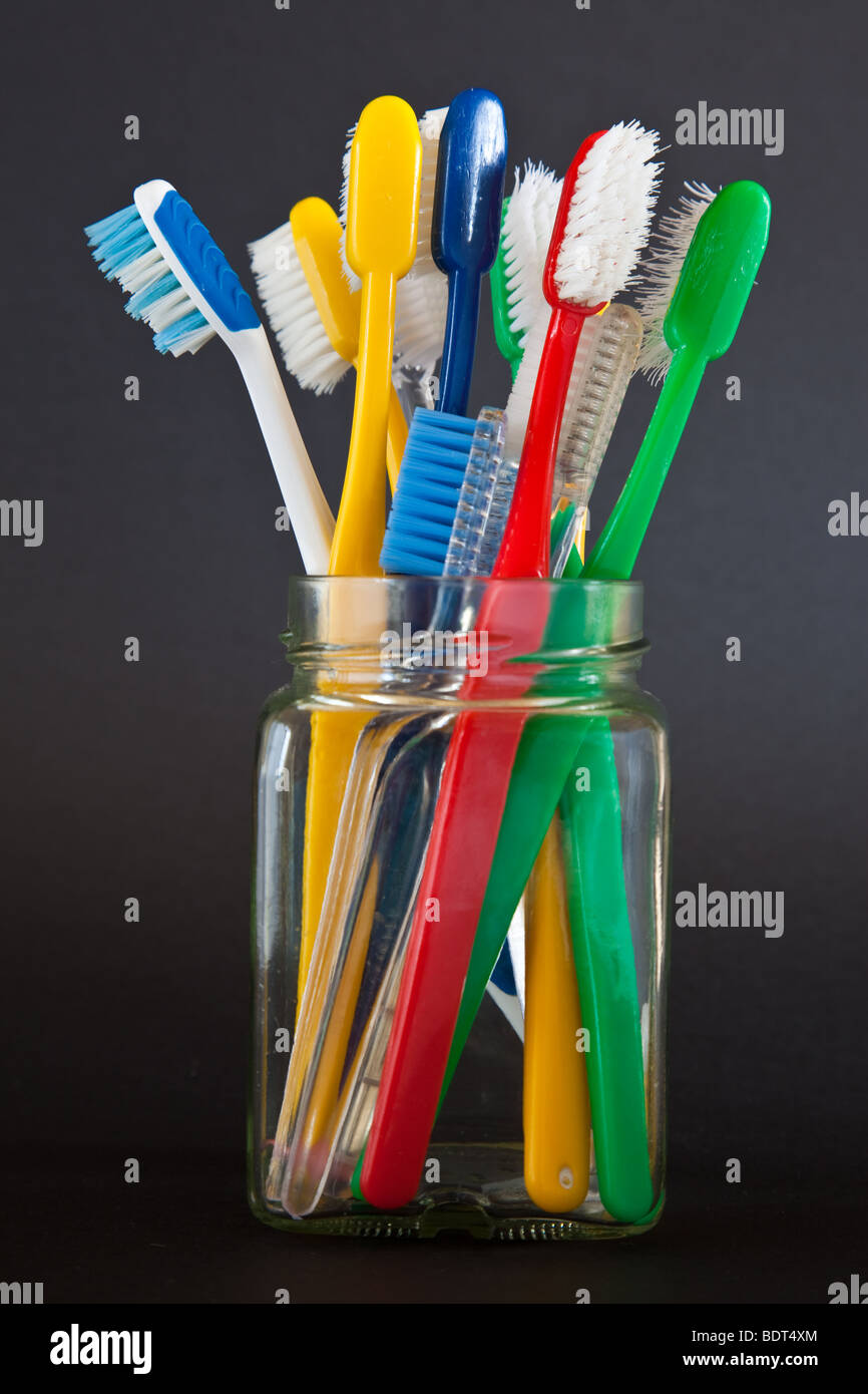 Alte Zahnbürsten von verschiedenen Farben in einem quadratischen Glas Marmelade Glas mit schwarzem Hintergrund Stockfoto