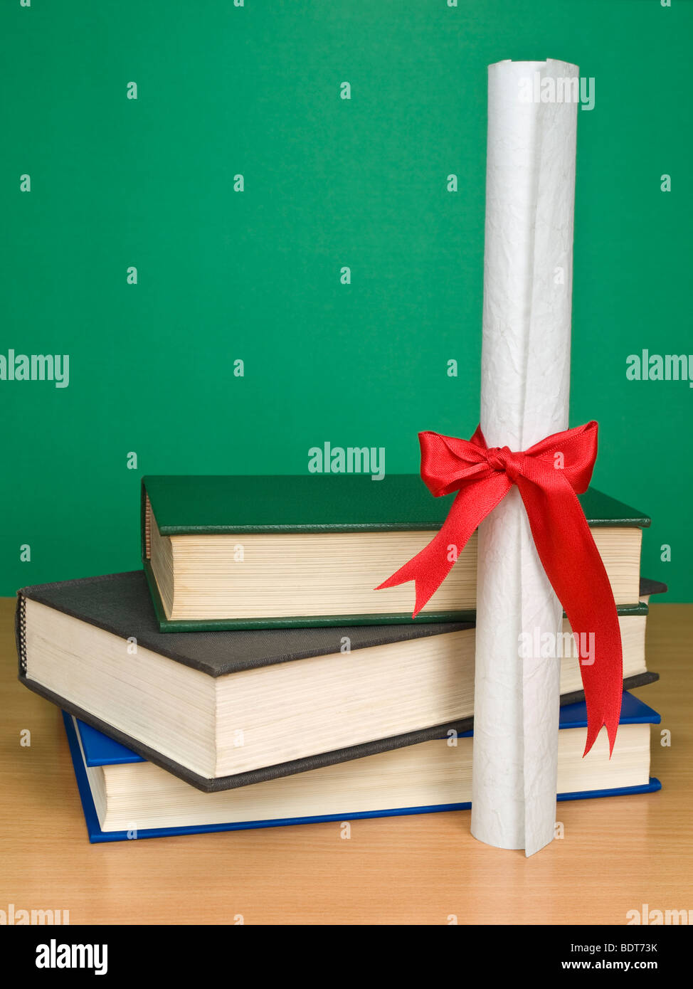 Ein Haufen Bücher und ein Diplom. Leere Tafel im Hintergrund. Stockfoto