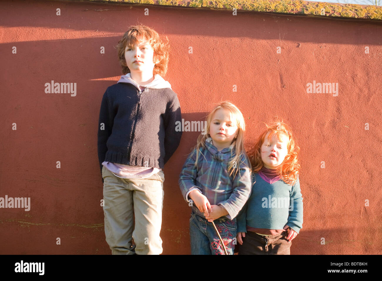 Bruder und zwei jüngere Schwestern stehend gegen eine Wand in der Sonne Stockfoto