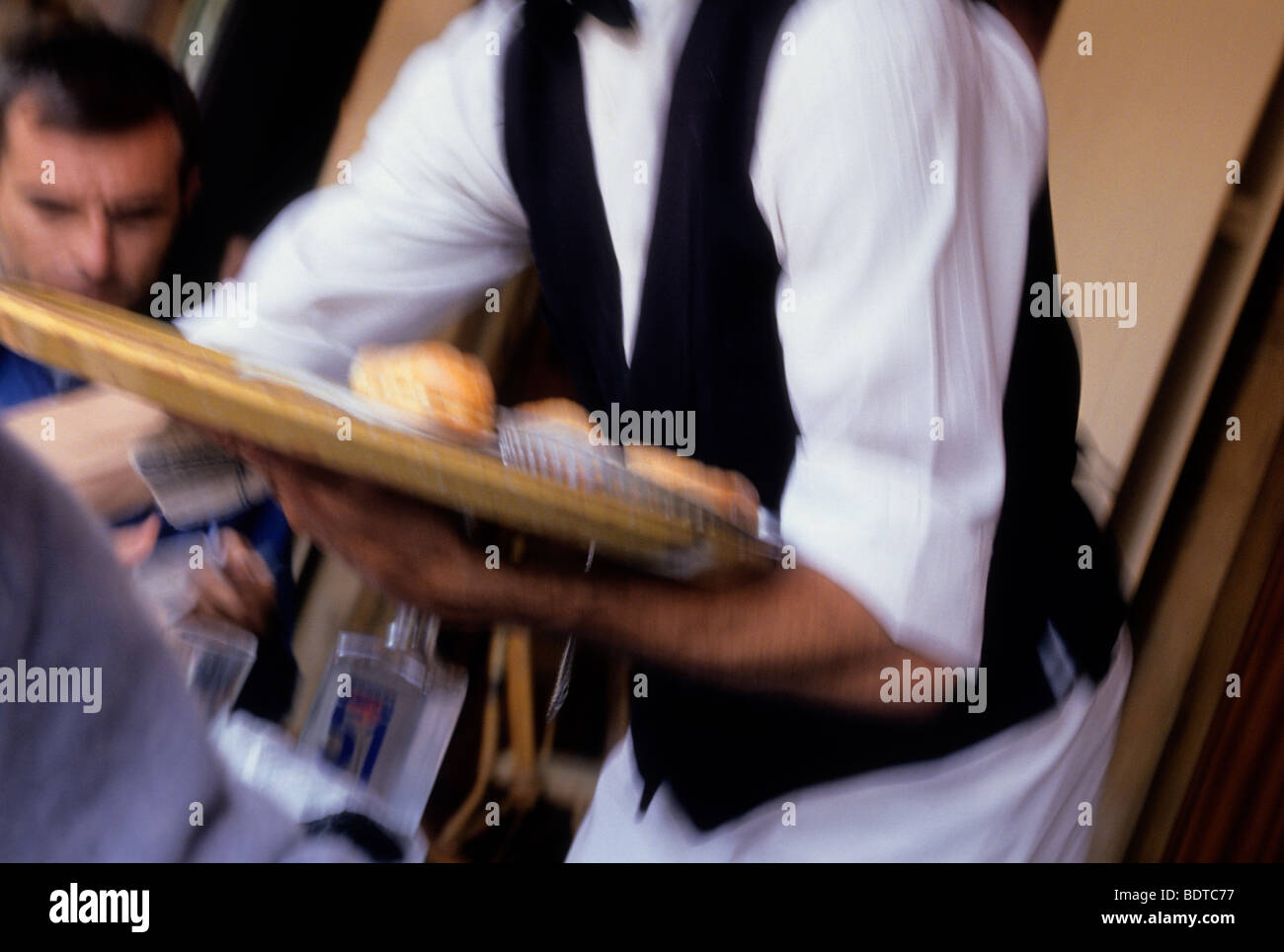 Paris Mittelteil des Kellners in einer schwarzen Weste, weißem Hemd und Schürze, der ein Tablett mit dem Essen balanciert. Nahaufnahme in Bistro, Café und Brasserie Stockfoto