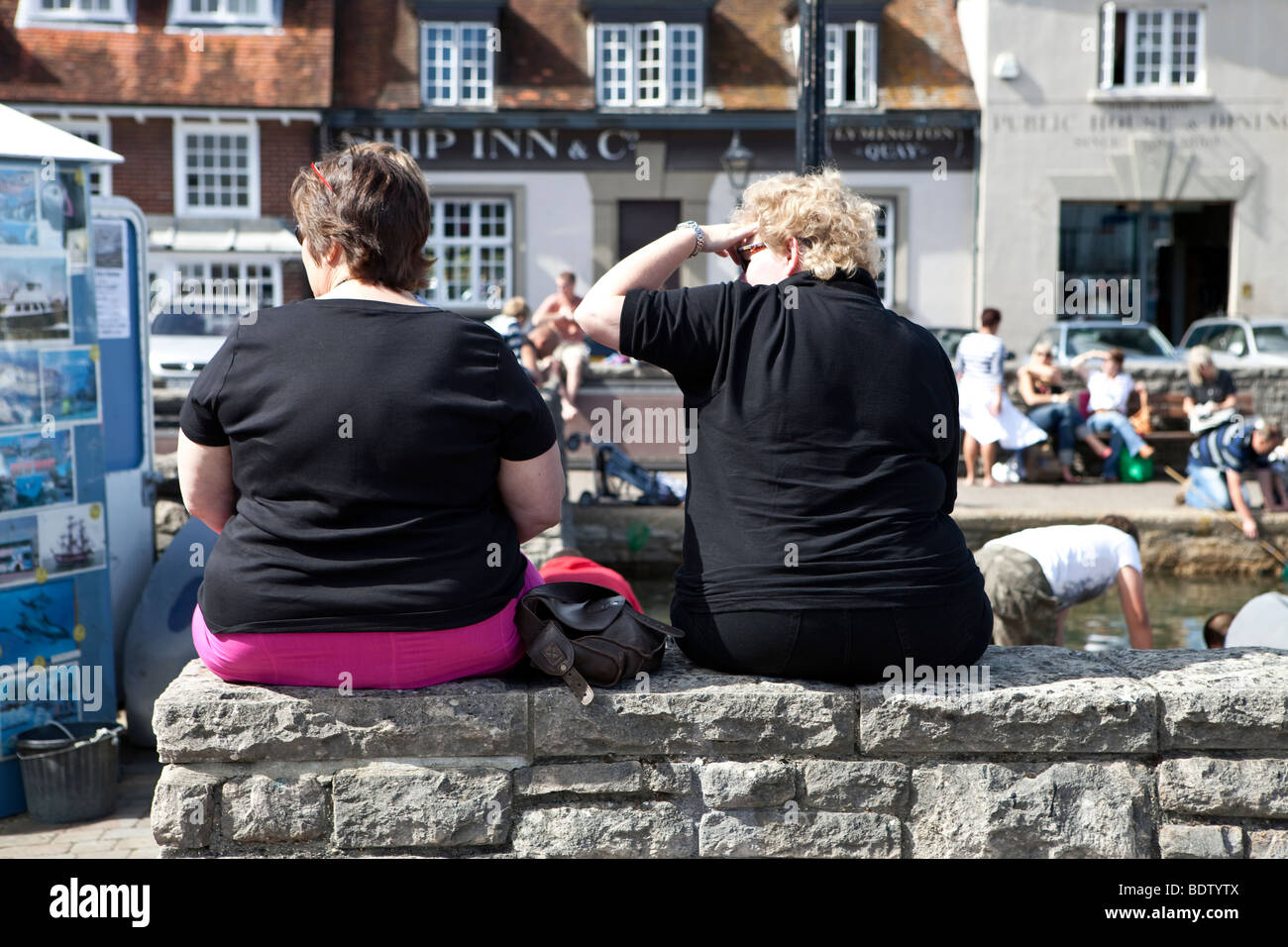 Zwei übergewichtige Frauen sitzen auf Wand in der Sonne. Stockfoto