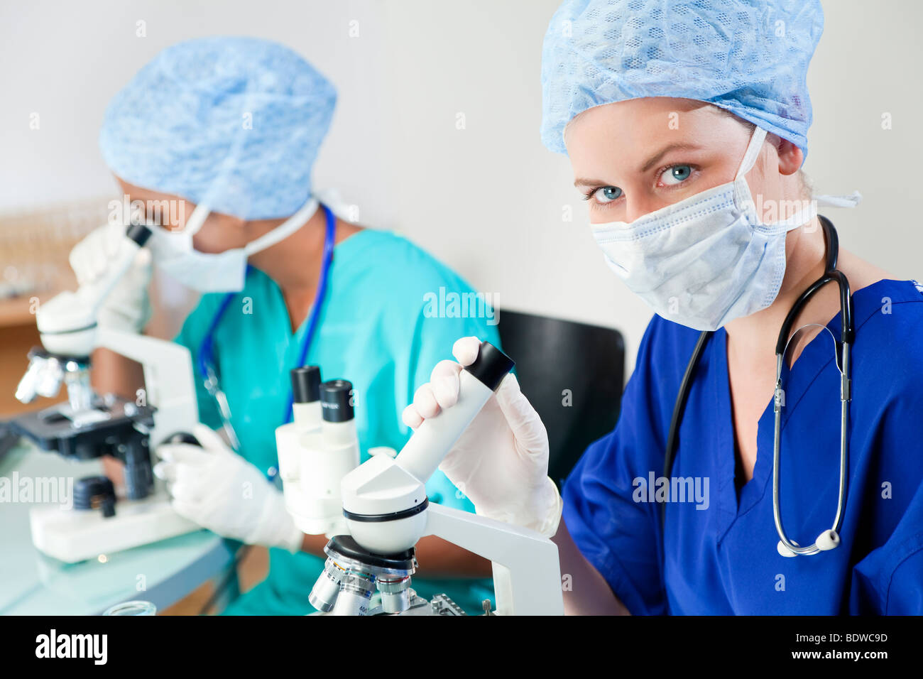 Eine blonde medizinische oder wissenschaftliche Forscherin oder Arzt mit ihrem Mikroskop im Labor mit ihrem asiatischen Kollegen Stockfoto