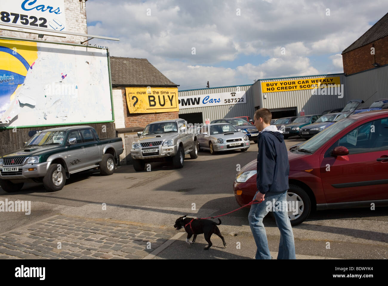 Ein junger Mann geht seinen Hund an der Leine rot vorbei an einem Autohaus in Hull. Stockfoto