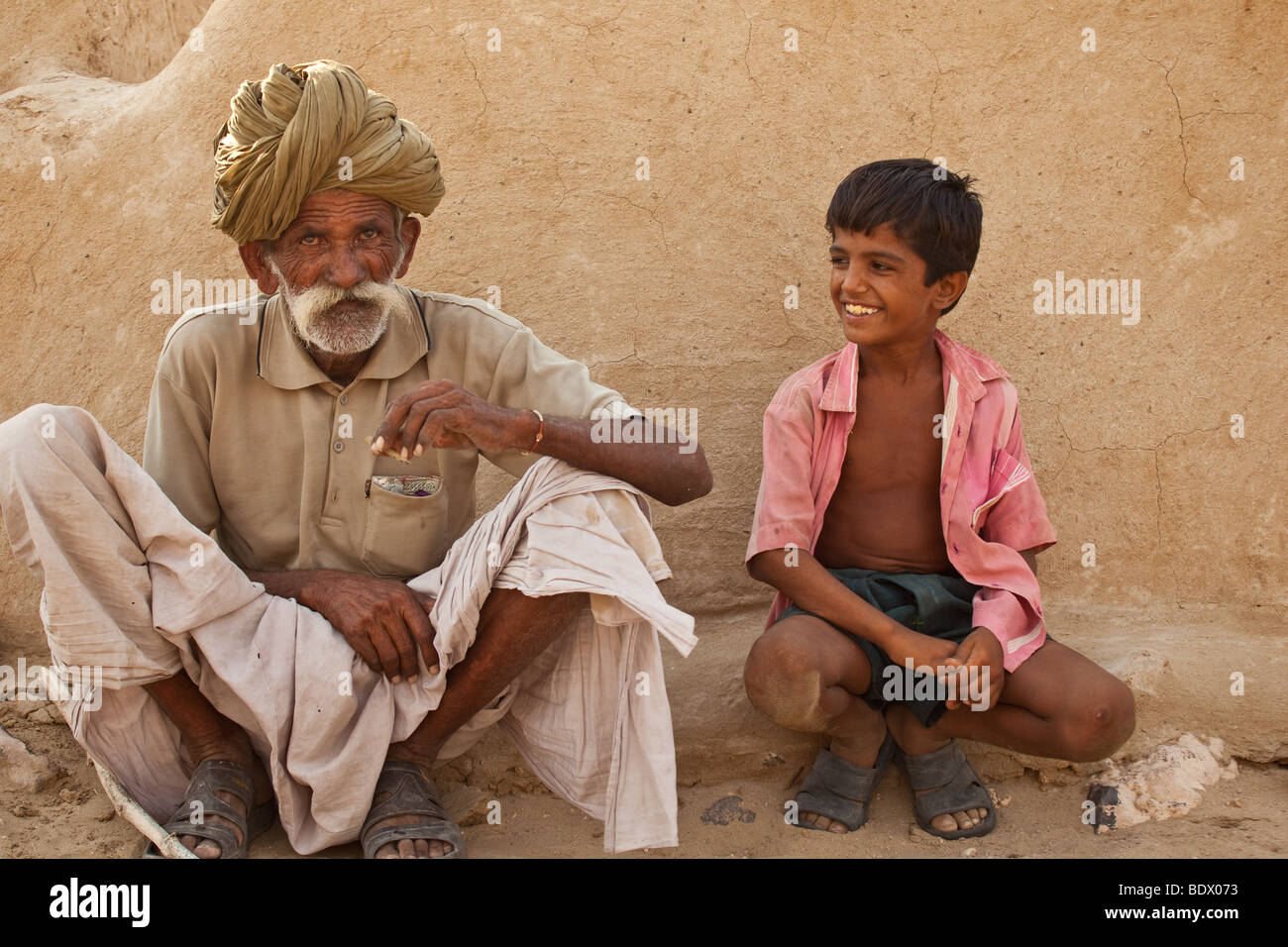 Wüste Thar, Indien eine alte Rajput Dorfbewohner beedi raucht eine Zigarette, während ein Junge lächelt und sieht auf. Stockfoto