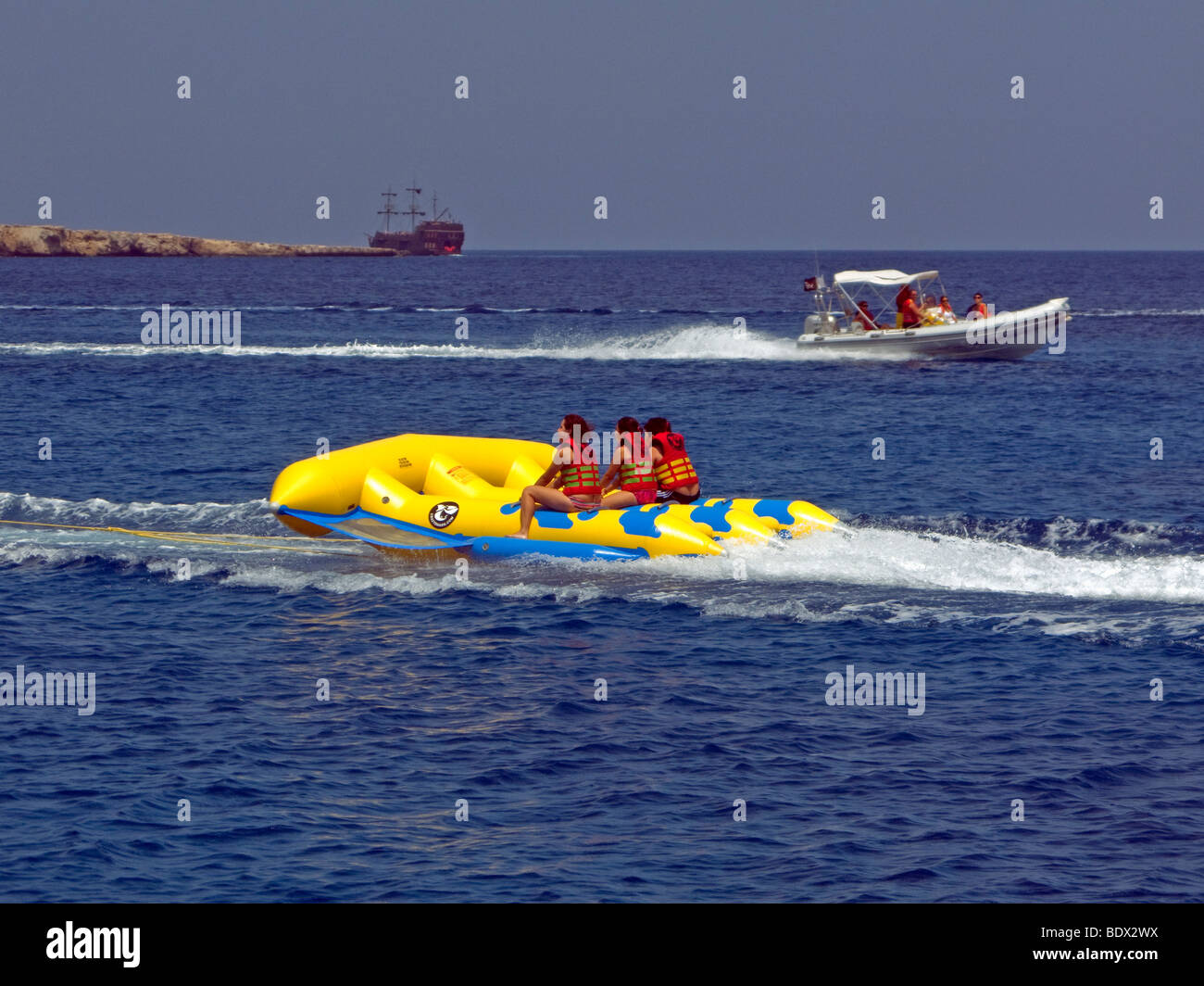 Touristen auf eine gelbe Flyfish aufblasbares Spielzeug von einem Motorboot gezogen in der Nähe von Ayia Napa, Zypern. Stockfoto
