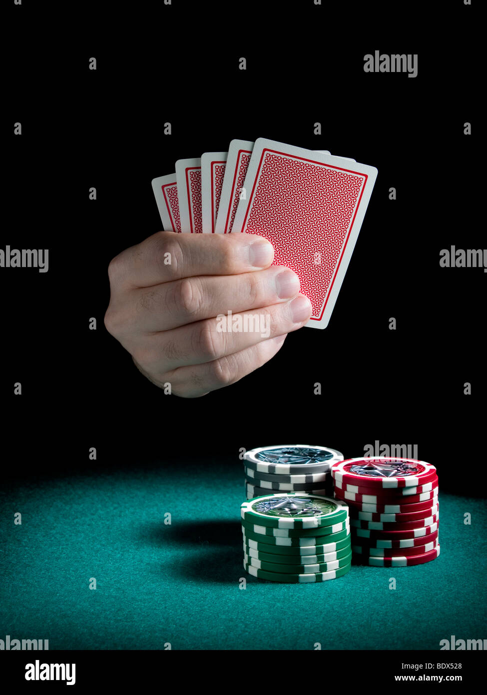 Eines Mannes Hand mit fünf Karten auf drei Pfähle Differents Farben Chips auf einer grünen Filz. Stockfoto