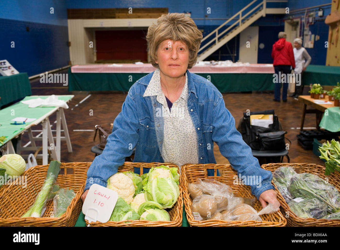 Eine mittlere gealterte Frau verkauft Gemüse auf einem Bauernmarkt in einer Halle statt. Stockfoto