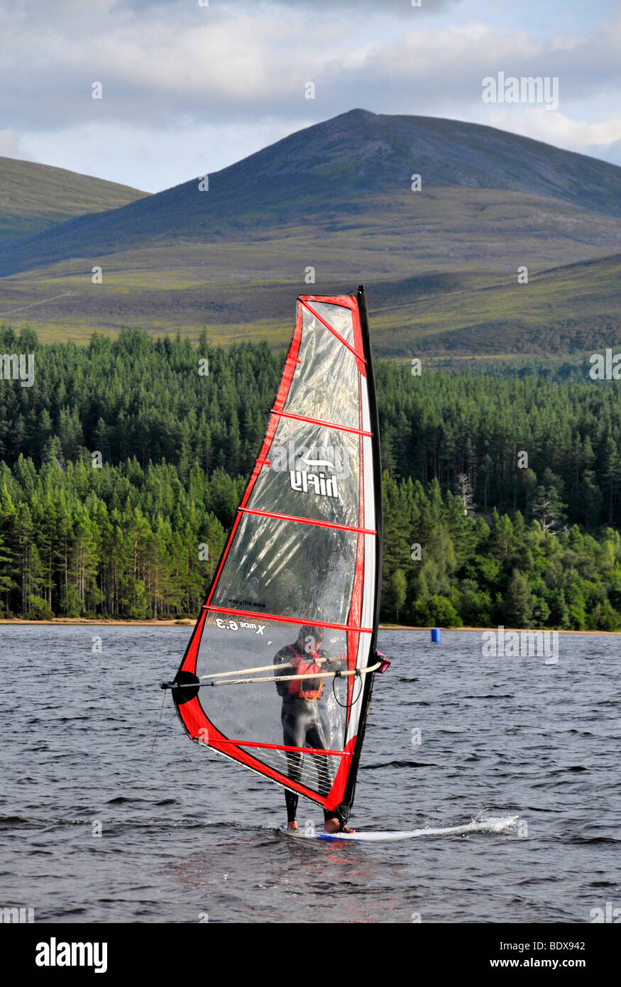 Ein Mann, Windsurfen am Loch Morlich, in der Nähe von Aviemore mit den Cairngorms im Hintergrund. Stockfoto