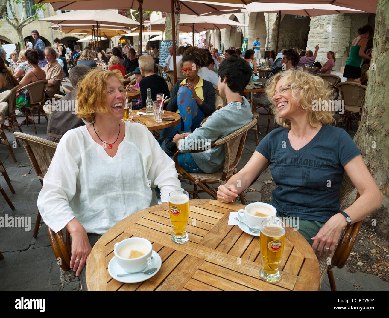 Zwei Frauen in den Vierzigern Lachen in einem Straßencafé auf den zentralen Platz Place Aux Herbes bei Uzès, Südfrankreich. Stockfoto