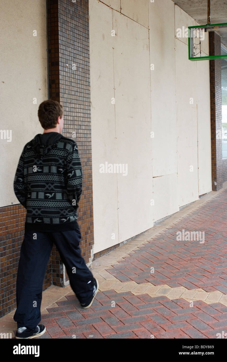 Junger Mann zu Fuß vorbei an Bord Shop auf kämpfenden High Street. Stockfoto