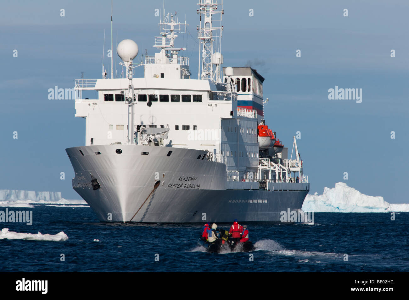 Eco - Touristen im Schlauchboot Zodiac Boot zurück zu verankert Expedition Kreuzfahrtschiff in der Antarktis, blauer Himmel, blaues Wasser, große Eisberge im Hintergrund Stockfoto