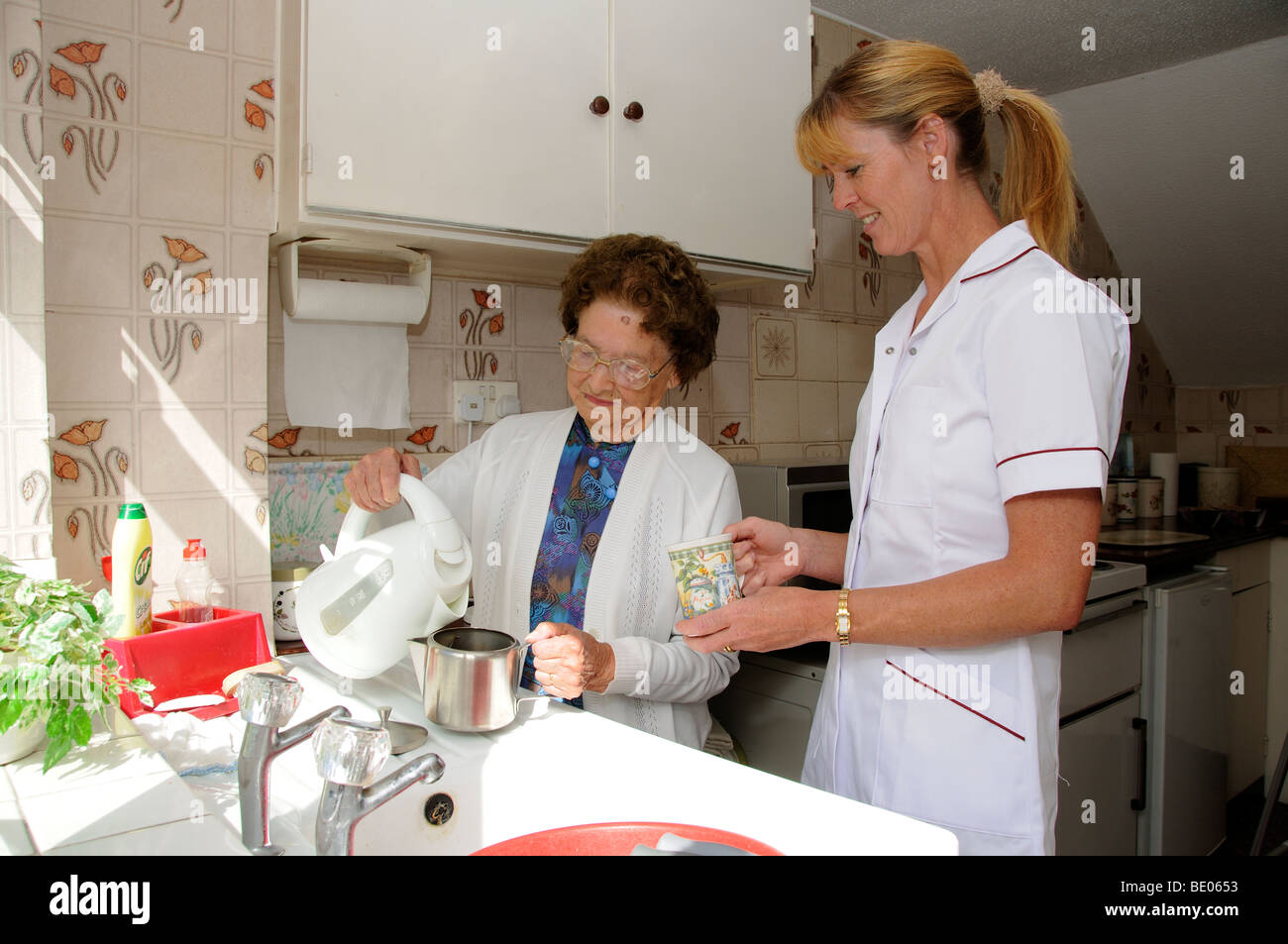 Ältere Frau in der Küche mit sozialen Diensten Betreuer gießt kochendes Wasser in eine Teekanne Stockfoto