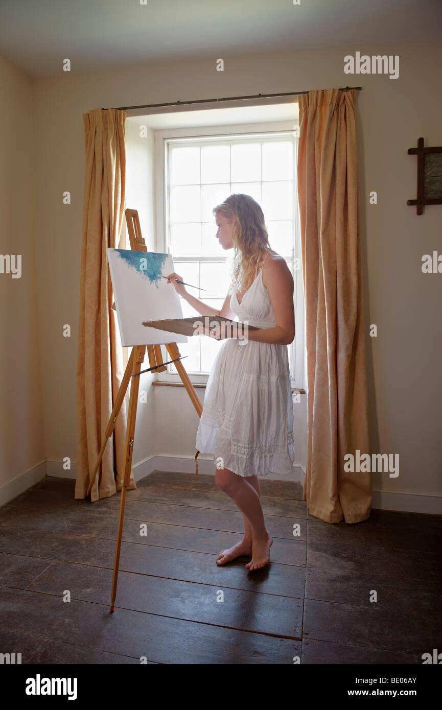 Junge Frau, die Gemälde von Fenster Stockfoto