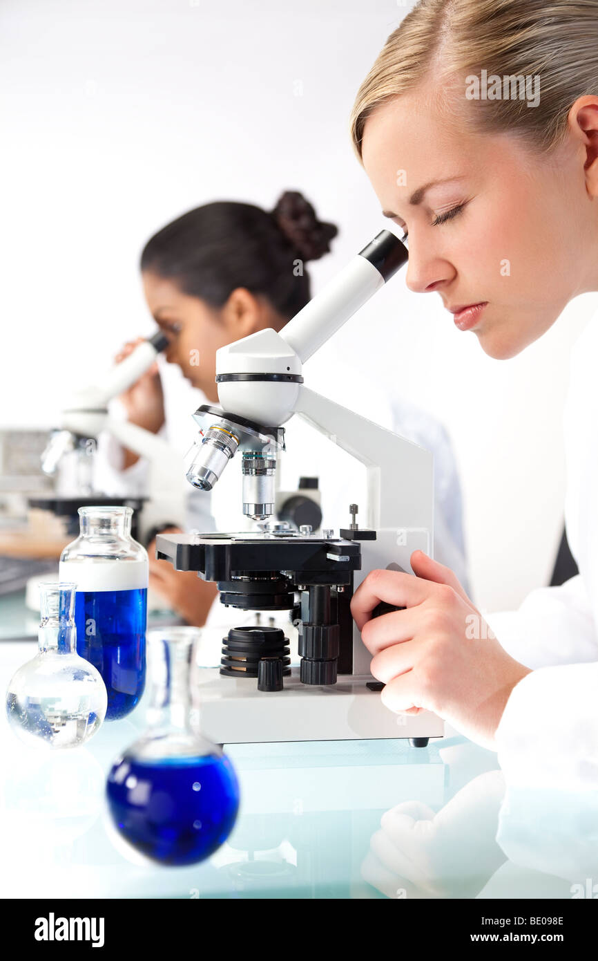 Eine blonde medizinische oder wissenschaftliche Forscherin oder Arzt mit ihrem Mikroskop im Labor mit ihrem asiatischen Kollegen Stockfoto