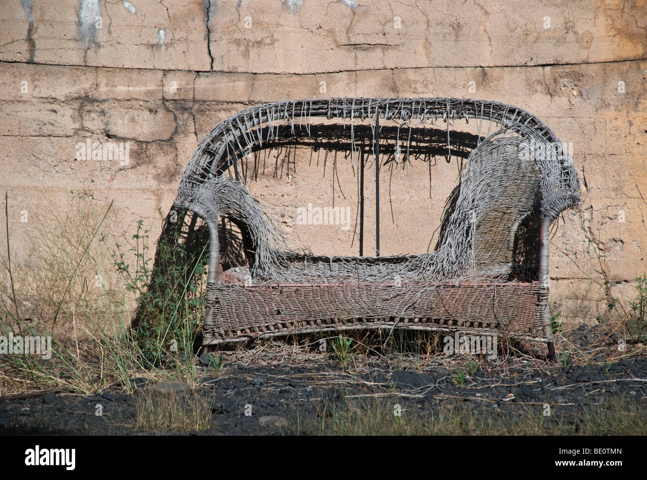 Ein Zweisitzer verwitterten Wicker sitzt allein durch eine sich verschlechternde Adobe-Wand in Chama, New Mexico. Stockfoto