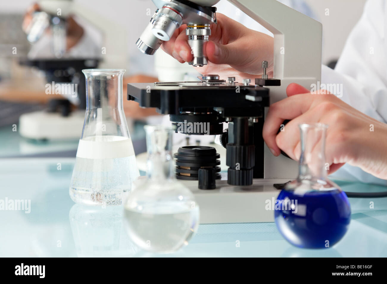 Eine medizinische oder wissenschaftliche Forscher unter Verwendung eines Mikroskops in einer Laborumgebung mit Fläschchen und medizinische Geräte. Stockfoto