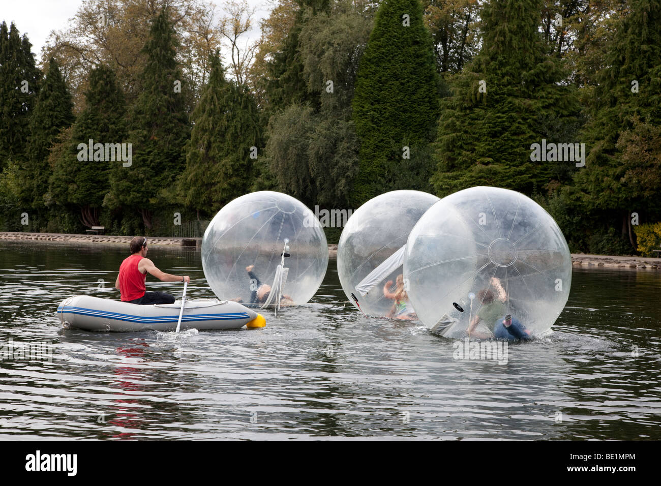Drei junge Mädchen spielen in einem Bubblerunner über den öffentlichen See bei Rouken Glen Park, Glasgow, UK, Schottland Stockfoto