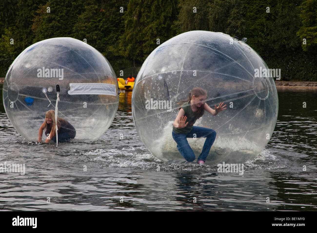 Zwei junge Mädchen spielen in einem Bubblerunner über den öffentlichen See bei Rouken Glen Park, Glasgow, UK, Schottland Stockfoto