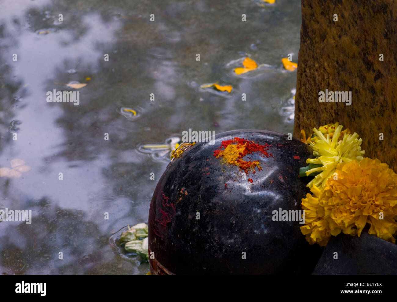 300 Jahre alten Shiva Lingum mit roten und gelben Heilige Pulver neben einen Stein mit Ringelblume Angebote Stockfoto