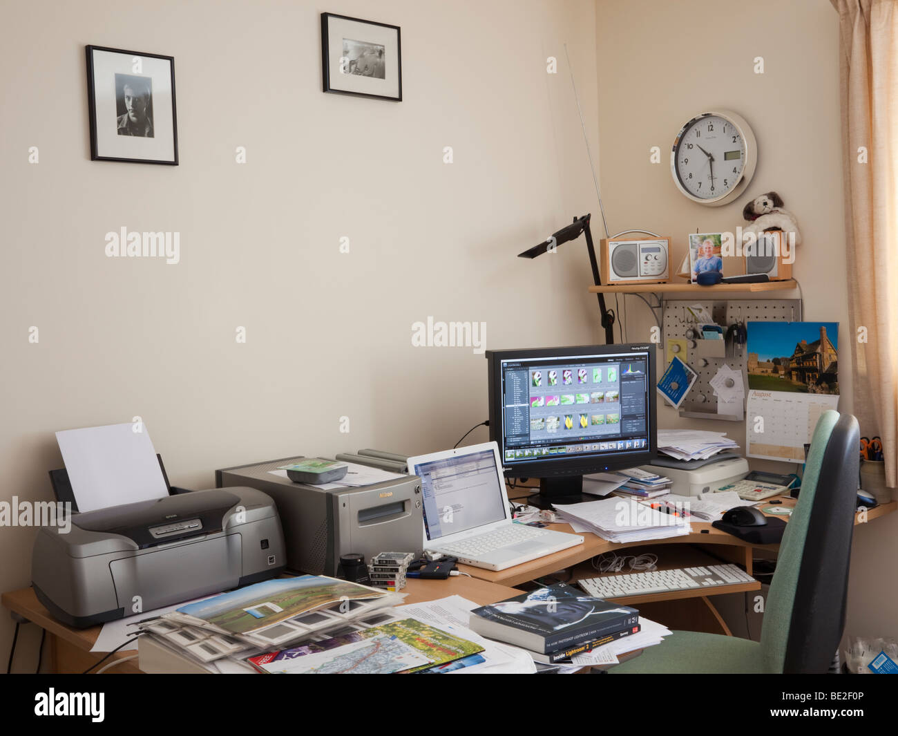 Fotografen im Büro zu Hause mit Laptop, Monitor, Lightroom, Drucker und Scanner auf einen unordentlichen Schreibtisch anzeigen. UK-Großbritannien Stockfoto