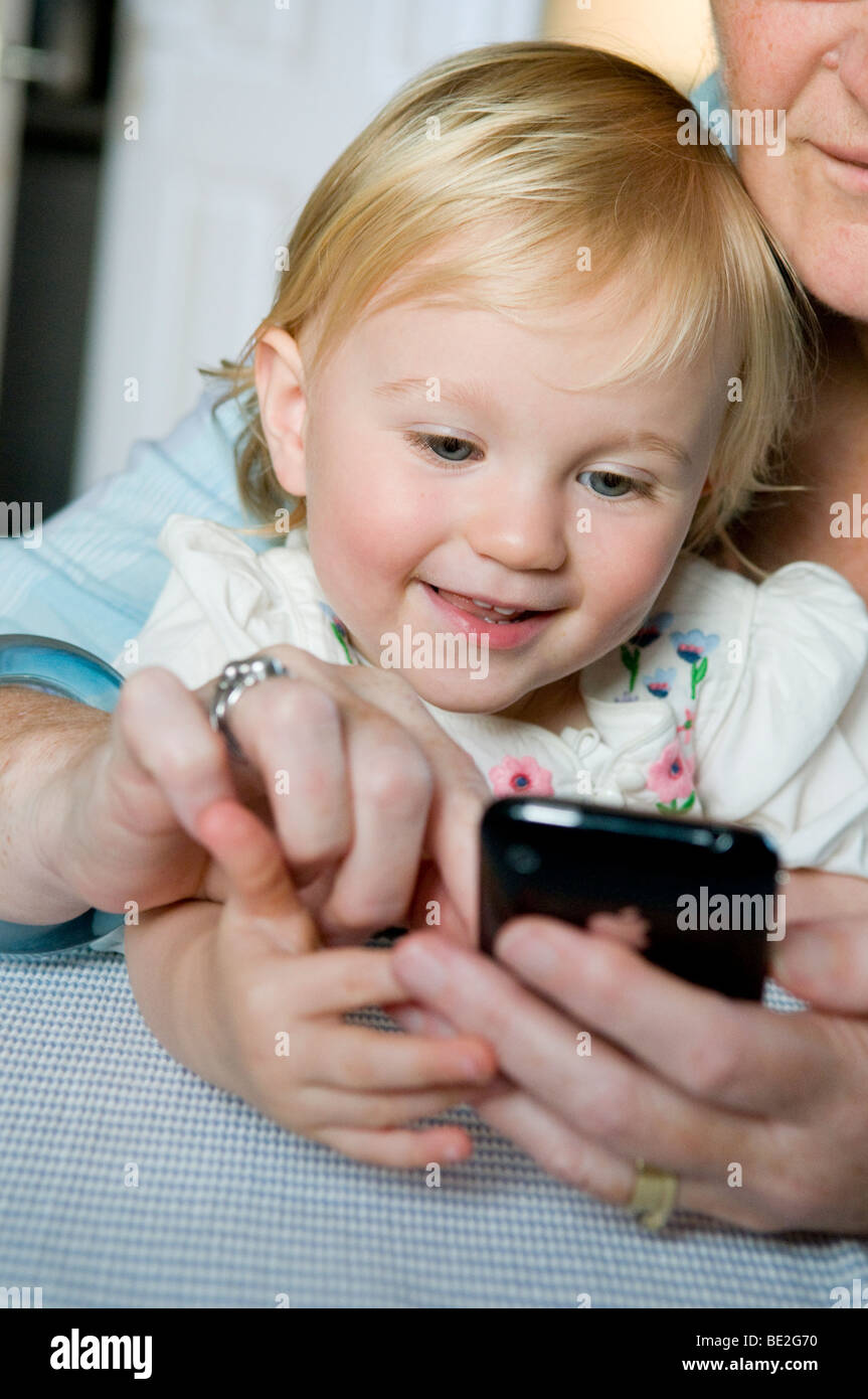 Baby Mädchen, Kleinkind, spielen mit einem Erwachsenen und ihrem Handy, einem Iphone. Stockfoto