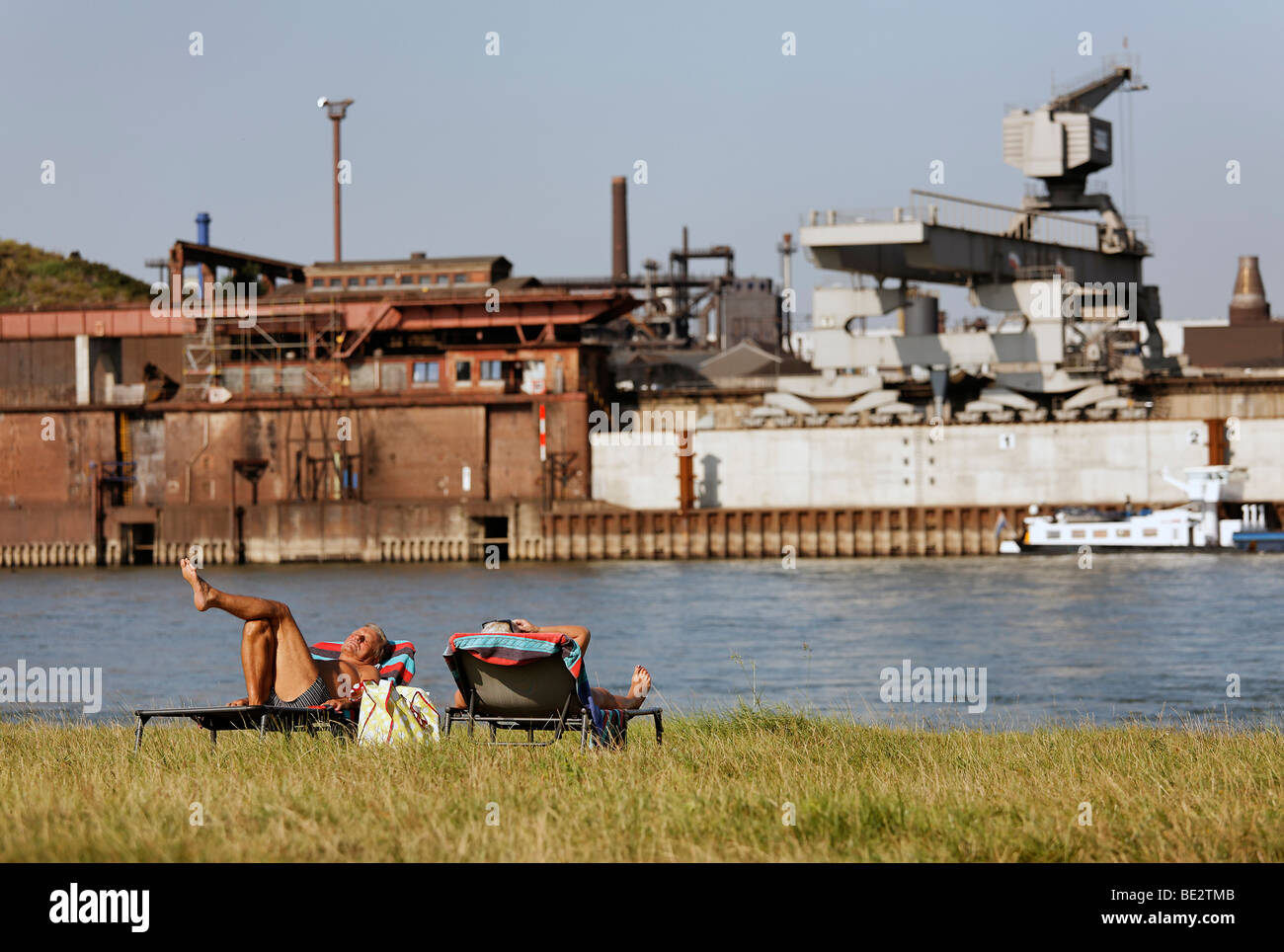 Zwei ältere Leute Sonnenbaden auf liegen an den Ufern des Rheins, Industriekulisse, Duisburg Kupfer Schmelzer, jetzt DK Stockfoto