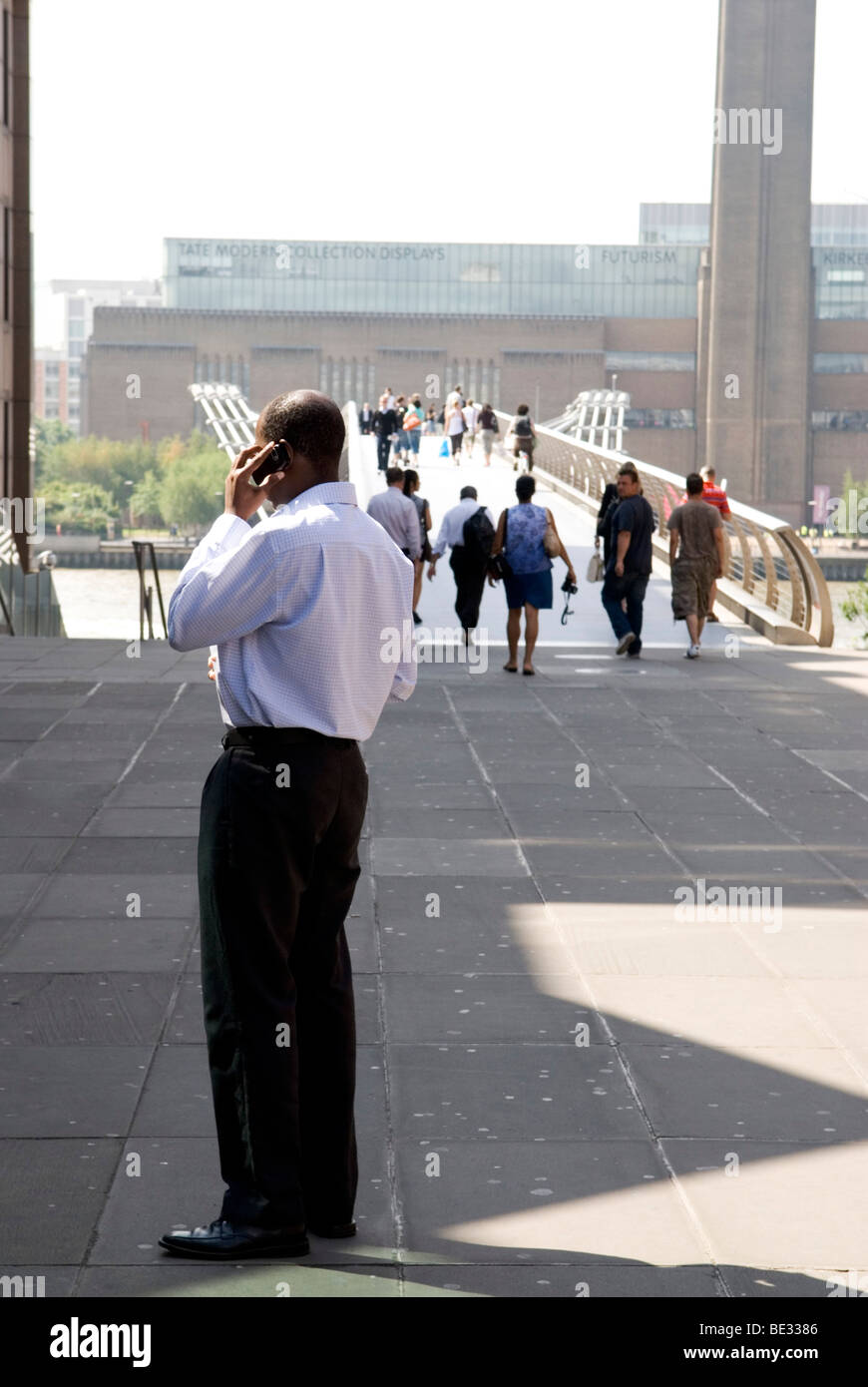 der Mensch steht während des Gesprächs auf dem Handy mit der Millennium Bridge und der Tate modern im Hintergrund Stockfoto