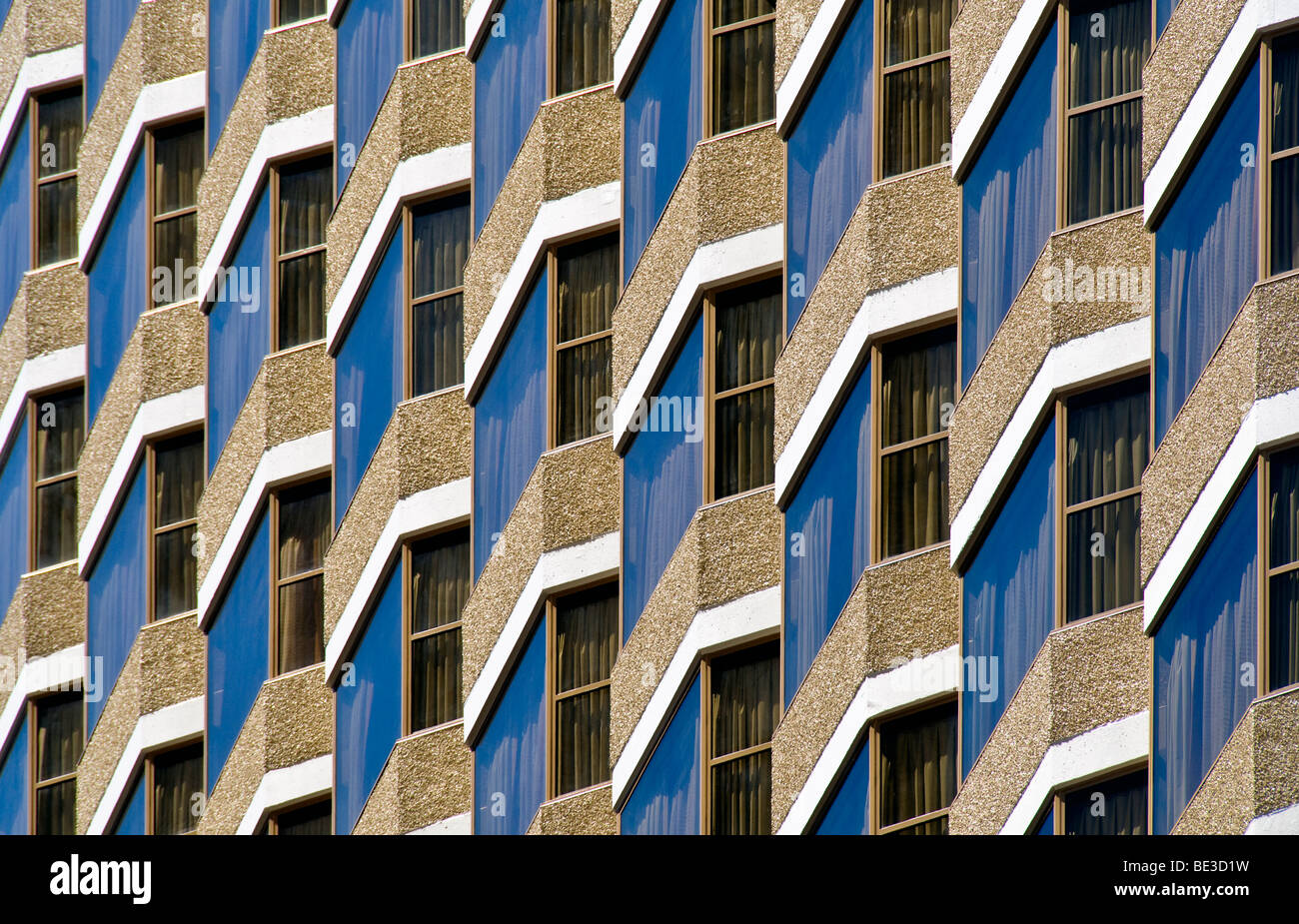 Gebäudefassade Geometrisches Design strukturierte Aggregatpaneele Reflektierende Fenster San Francisco Kalifornien // SAN FRANCISCO, Kalifornien – Eine Nahaufnahme einer modernen Gebäudefassade in San Francisco, Kalifornien, zeigt ein unverwechselbares geometrisches Design. Die Fassade besteht aus dunklen, reflektierenden Fenstern, die den blauen Himmel spiegeln und einen beeindruckenden visuellen Effekt erzeugen. Diese Fenster sind präzise in strukturierten, hellen Zuschlagplatten angeordnet. Scharfe, weiße eckige Rahmen definieren die Kanten jedes Fensterabschnitts und betonen den zeitgenössischen architektonischen Stil des Gebäudes. Dieses komplizierte Muster (Fortsetzung Stockfoto