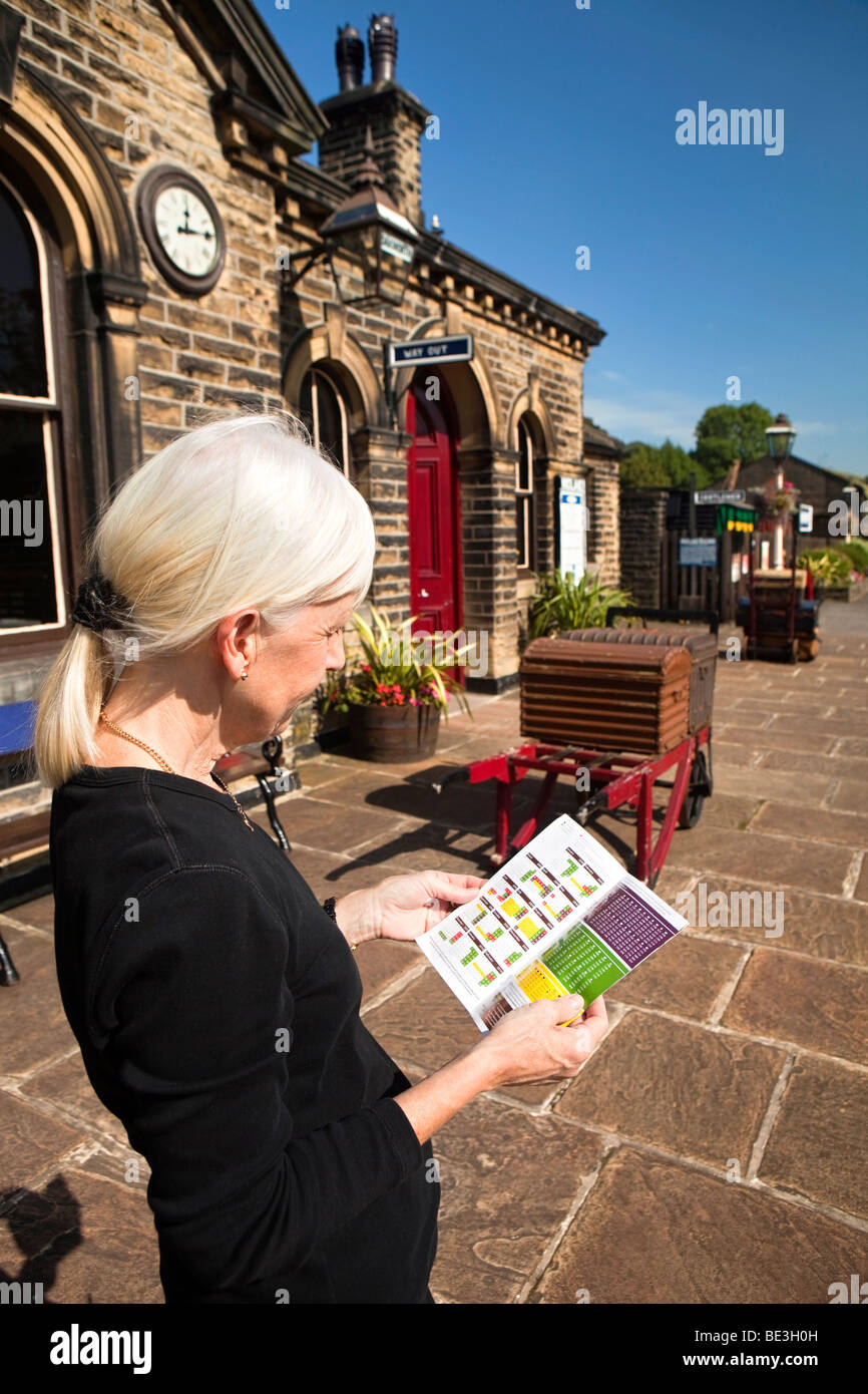 Großbritannien, England, Yorkshire, Keighley und Wert Valley Railway, Frau wartet auf Oakworth Bahnsteig Blick auf Zug Fahrplan Stockfoto