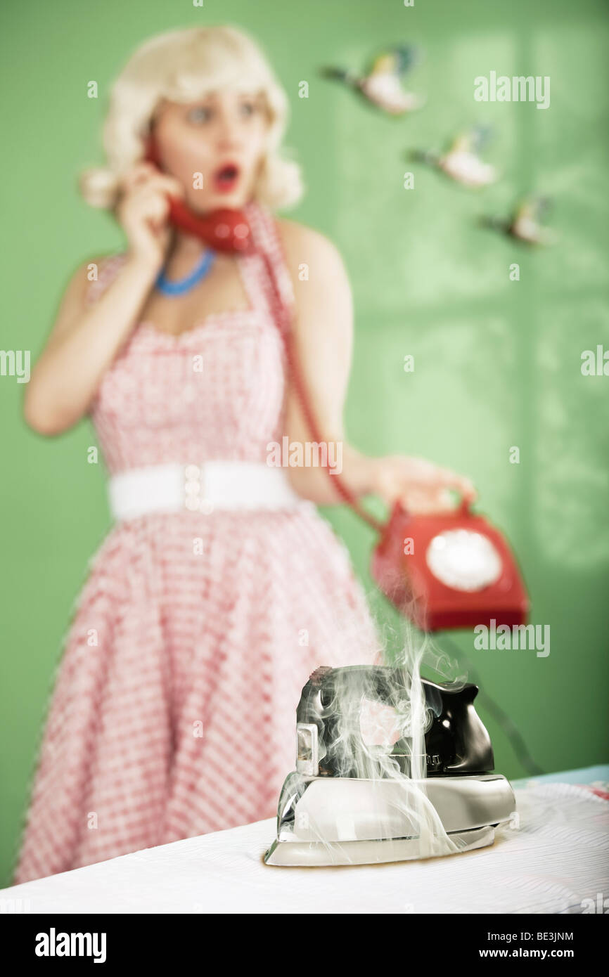 Retro-Hausfrau am Telefon, mit Eisen brennen ein Hemd im Vordergrund. Stockfoto