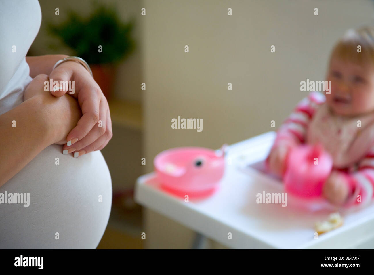 Schwangere Frau, die Hände auf den Bauch mit Kind im Hochstuhl Stockfoto