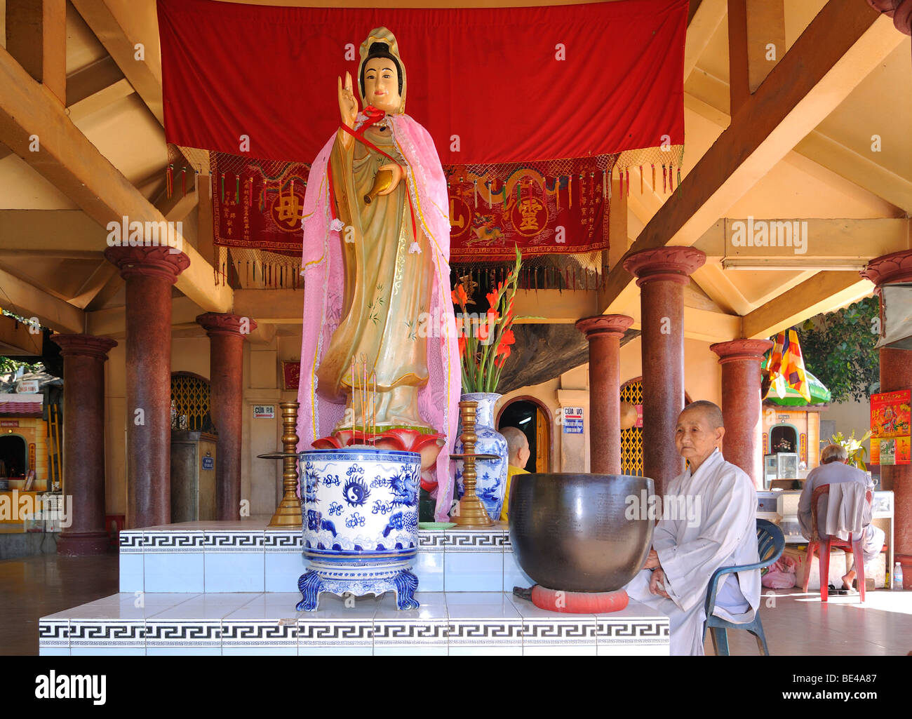 Nonne sitzt neben einer Statue in einem Tempelkomplex auf dem Black Mountain, Vietnam, Asien Stockfoto