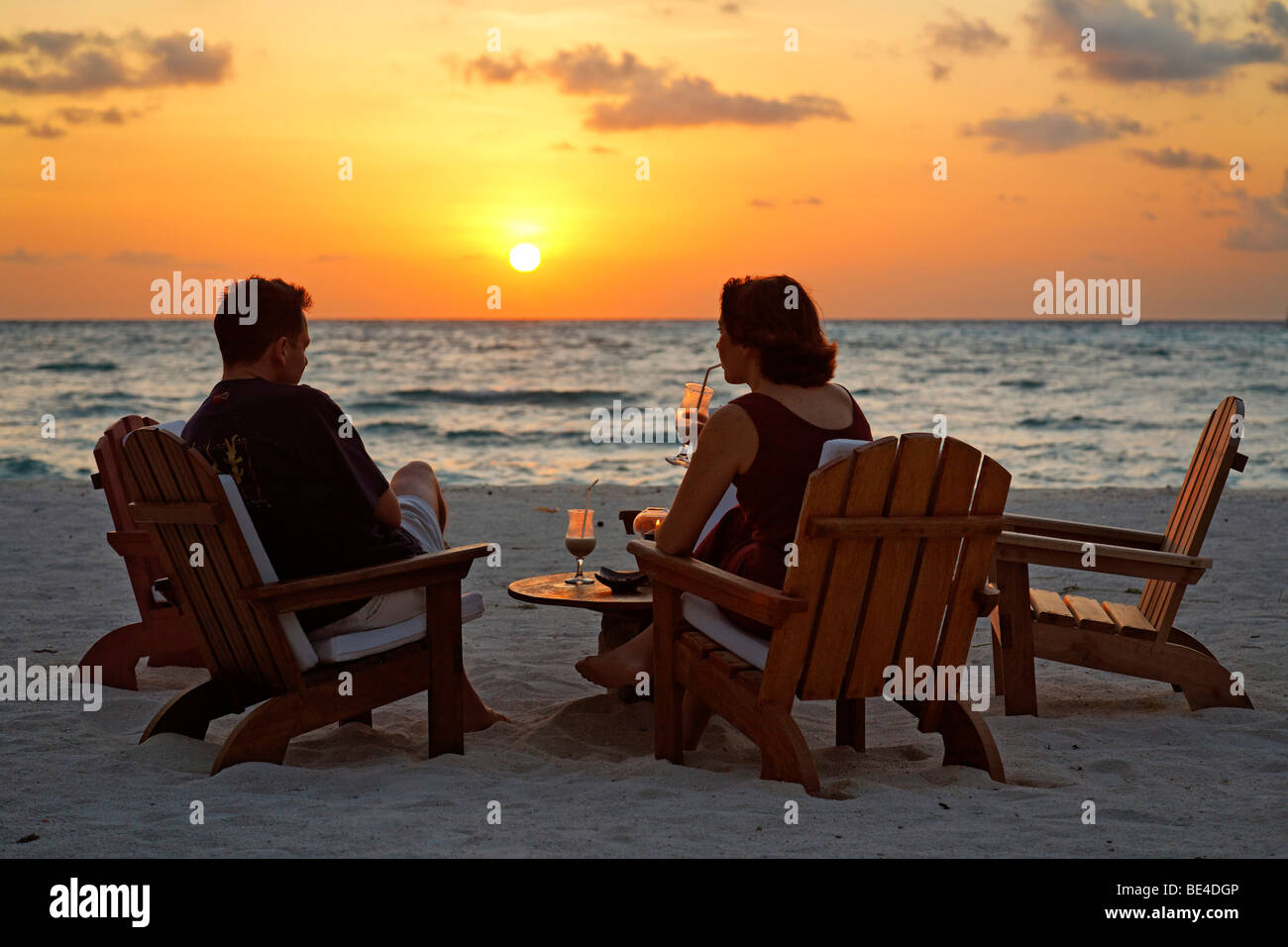 Paar, sitzen auf Stühlen am Strand mit Longdrinks vor einen goldenen Sonnenuntergang, Rihiveli, Insel, Malediven, Süd Male Ato Stockfoto