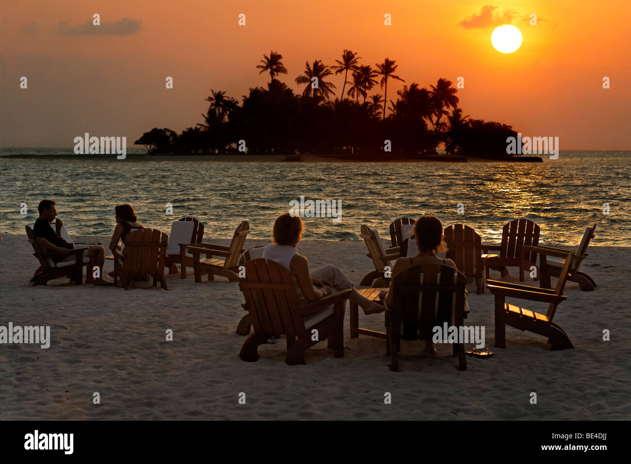 Menschen sitzen auf Stühlen am Strand mit Longdrinks vor einen goldenen Sonnenuntergang Malediven Insel, Rihiveli, Insel, Mald Stockfoto