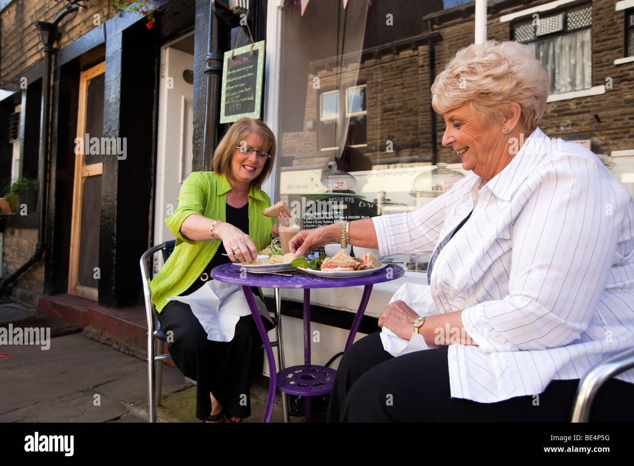 Großbritannien, England, Yorkshire, Haworth, Main Street, zwei Frauen, die Sandwich-Lunch draußen im Straßencafé genießen Stockfoto