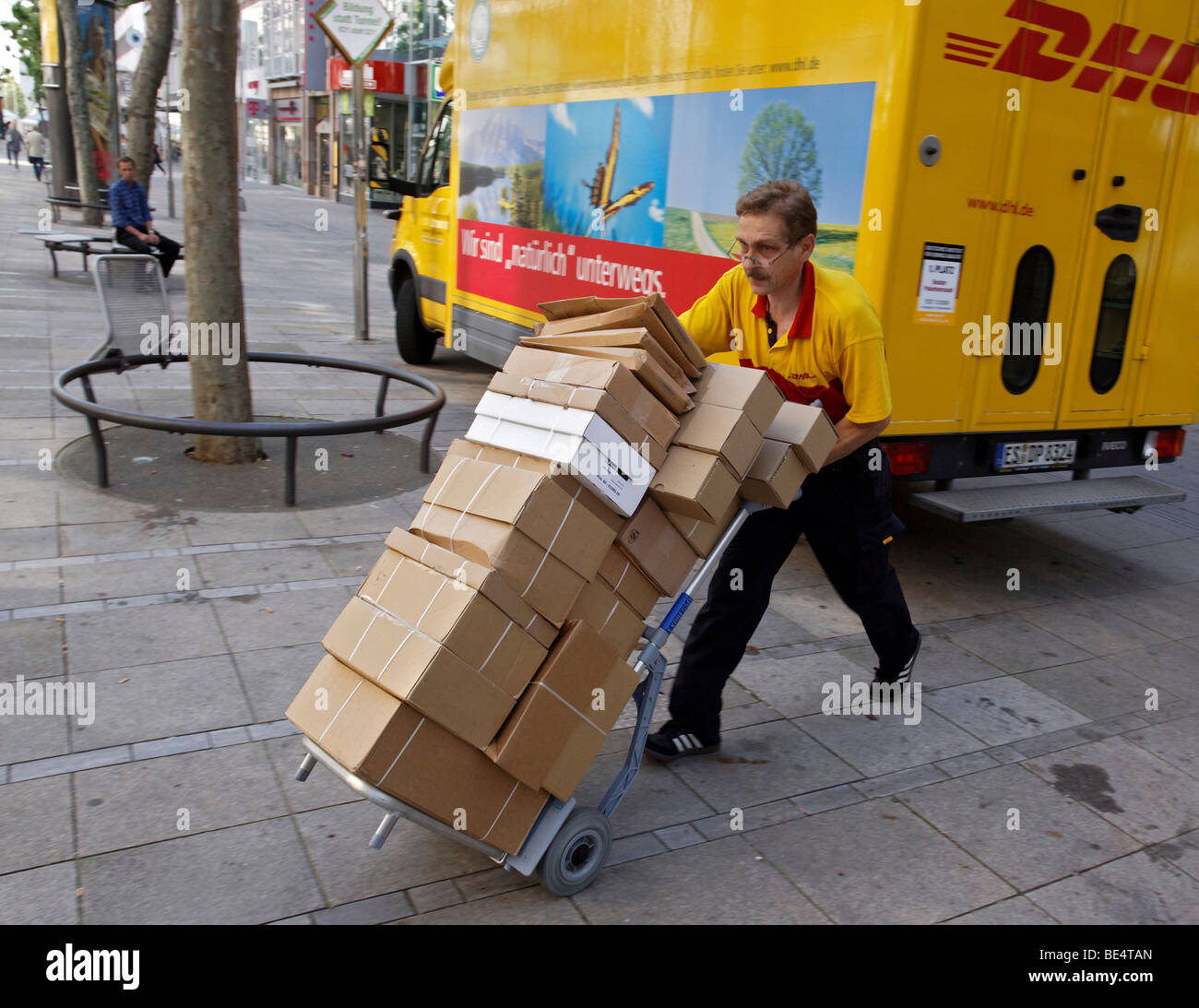 Paket-Träger Michael Meindel Ausgleich einen Stapel von Paketen auf der anderen Straßenseite mit seinem Karren für die Deutsche Post Deutsche Post Stockfoto
